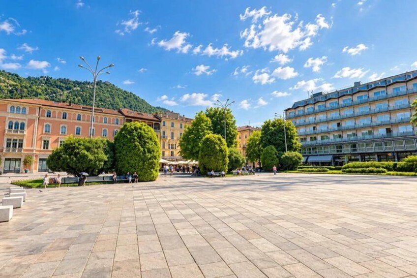 A spacious square with trees, buildings, and a clear sky. 2