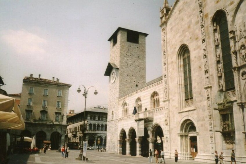 A historic square with a prominent clock tower, arched buildings, and a clear sky. 4
