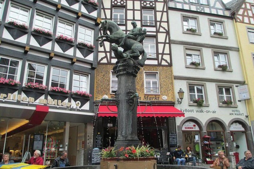 A town square with a statue, buildings with signs, and people sitting at tables. 3