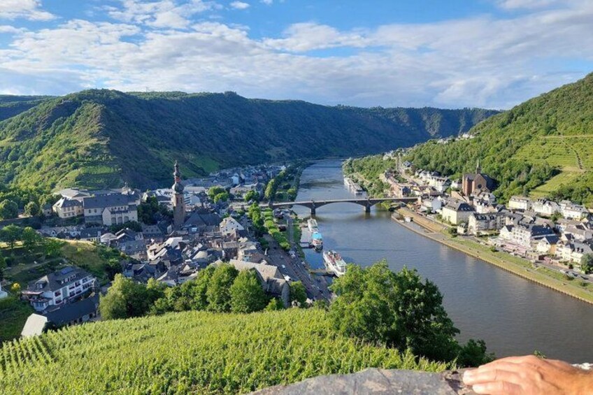 A town by a river with a bridge, vineyards, and hills. 1