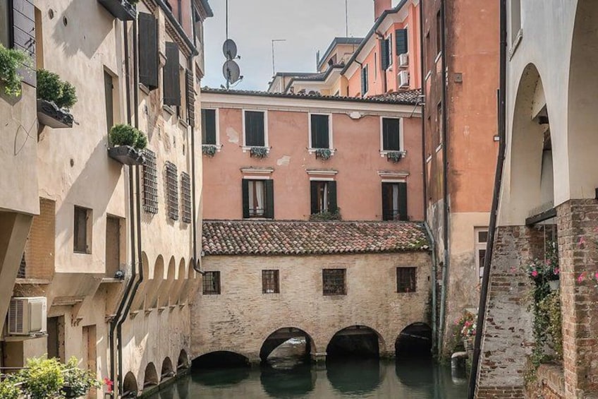 A narrow canal with buildings on either side, a bridge, and a clear sky. 3