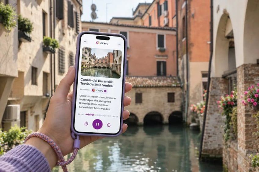 A person holding a smartphone displaying a canal view with historic buildings. 1