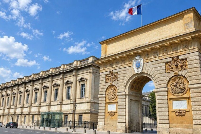 A historic stone building with a large archway, a flag, and a coat of arms. 5