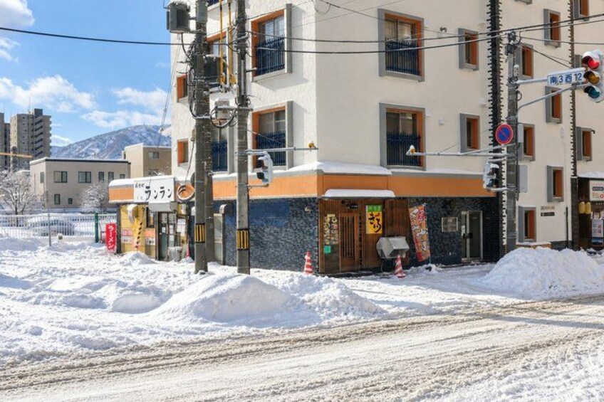 A building with a sign that reads 'ラーメン' in front of a snow-covered street. 4