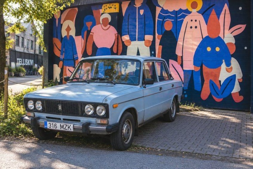 A vintage blue car parked in front of a colorful mural. 5