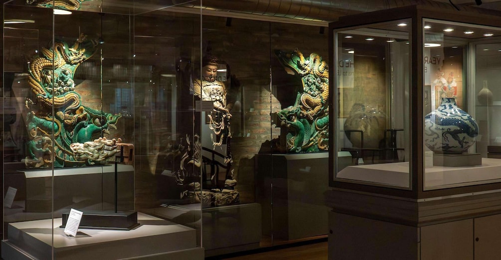A museum display with glass cases containing ornate sculptures and a blue and white vase. 2