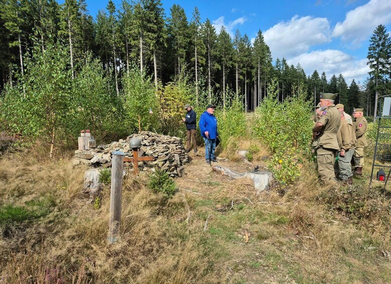 A group of people in a forested area with a stone structure and a metal fence. 1