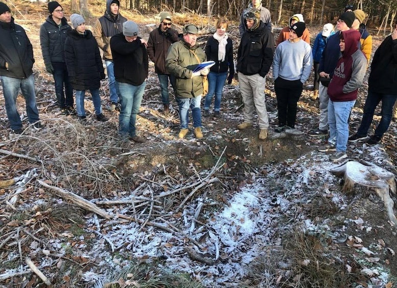 A group of people standing in a snowy outdoor area with bare trees and a fallen tree trunk. 2