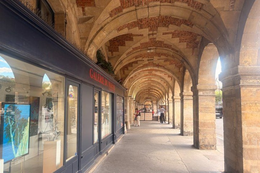 A covered walkway with arches, a storefront with a sign reading 'GALERIE DU MARSEILLE,' and a clear sky. 5