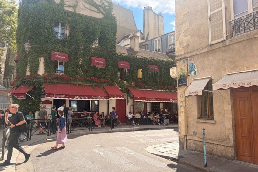 A street with cafes, pedestrians, and a building with ivy. 3