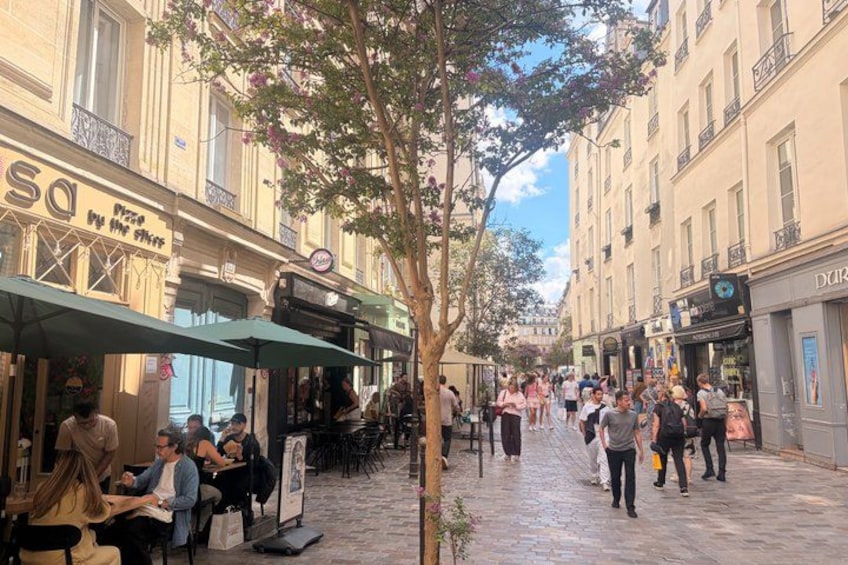A tree-lined cobblestone street with outdoor cafes and pedestrians. 2