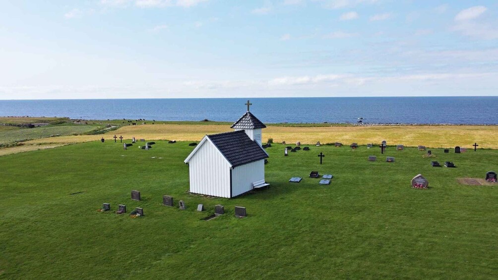 En kirkegård med en hvid kirke og kors, foran et kystlandskab. 3