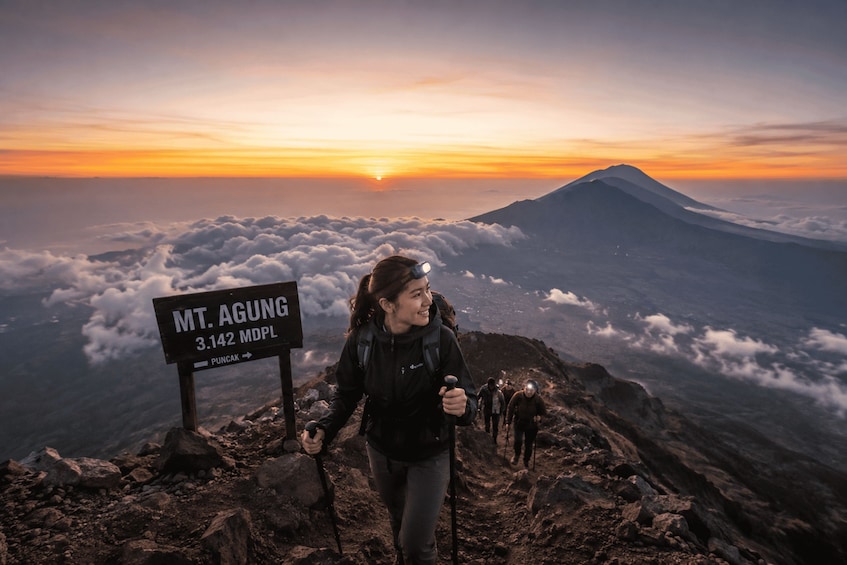 A hiker at the summit of a mountain with a sign indicating the name and elevation. 4