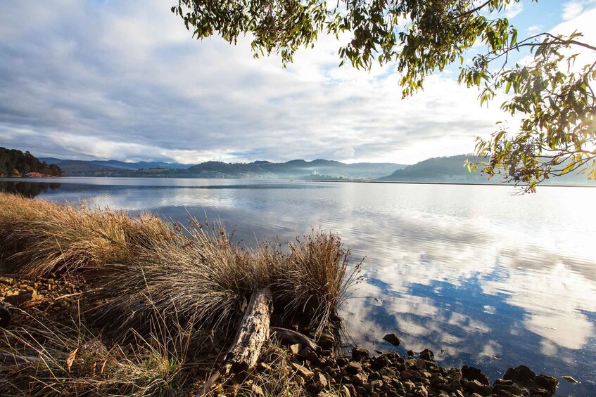 A calm lake with a rocky shoreline, surrounded by hills and a cloudy sky. 5