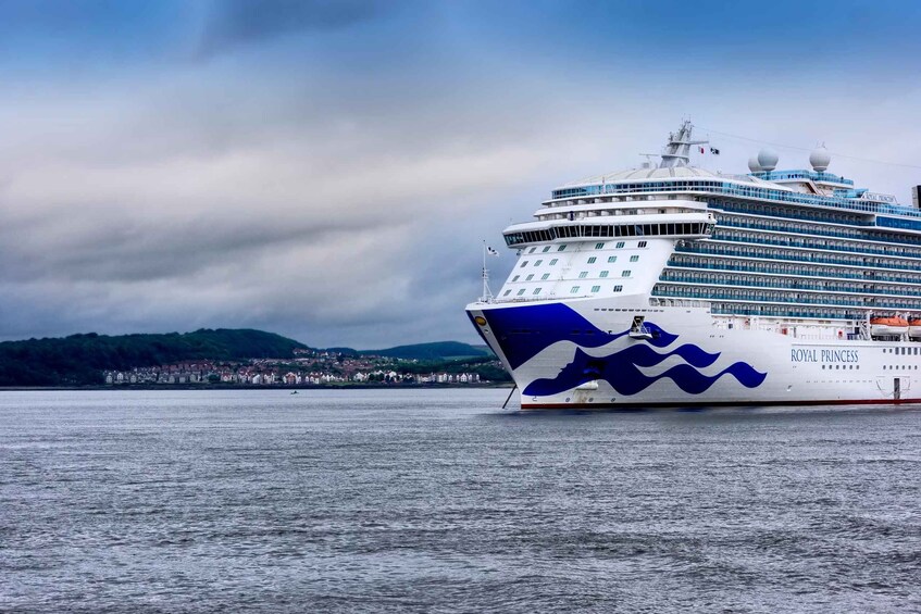 A large cruise ship named Royal Princess docked at a port with a backdrop of a cloudy sky and a hilly landscape. 3