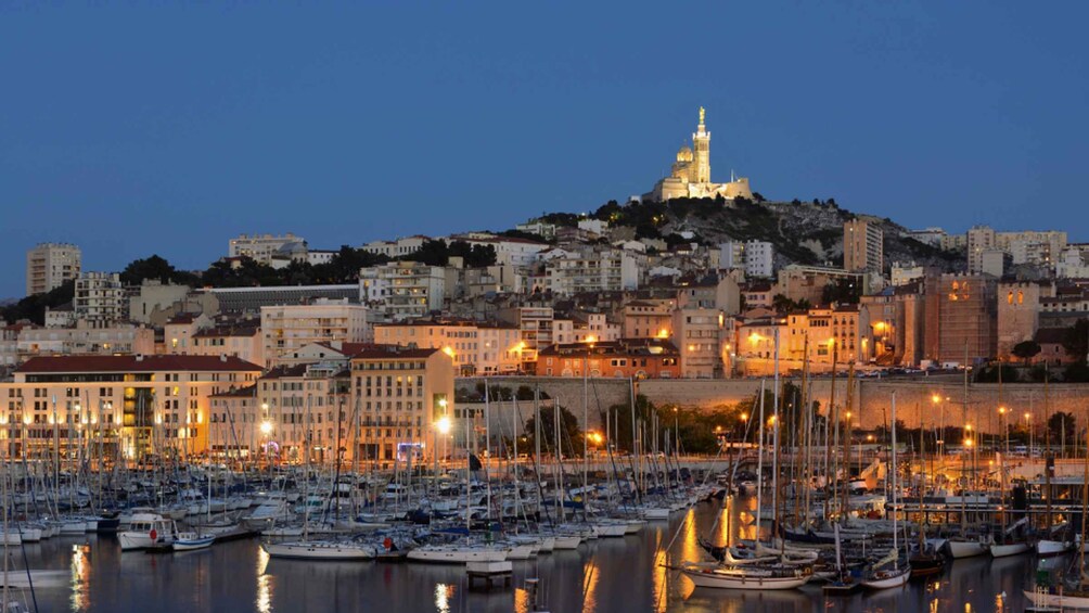 A marina with numerous boats docked, a cityscape with buildings, and a prominent hilltop structure with a tower. 2