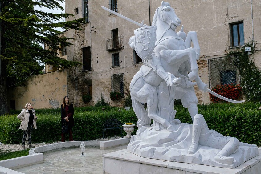 Una estatua ecuestre blanca en un patio con una fuente, rodeado de vegetación y edificios antiguos. 2