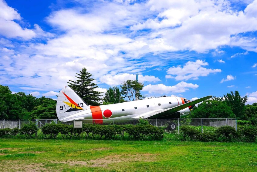 Un avión antiguo con diseño rojo y blanco, estacionado en un campo con césped, árboles y un cielo despejado de fondo. 4