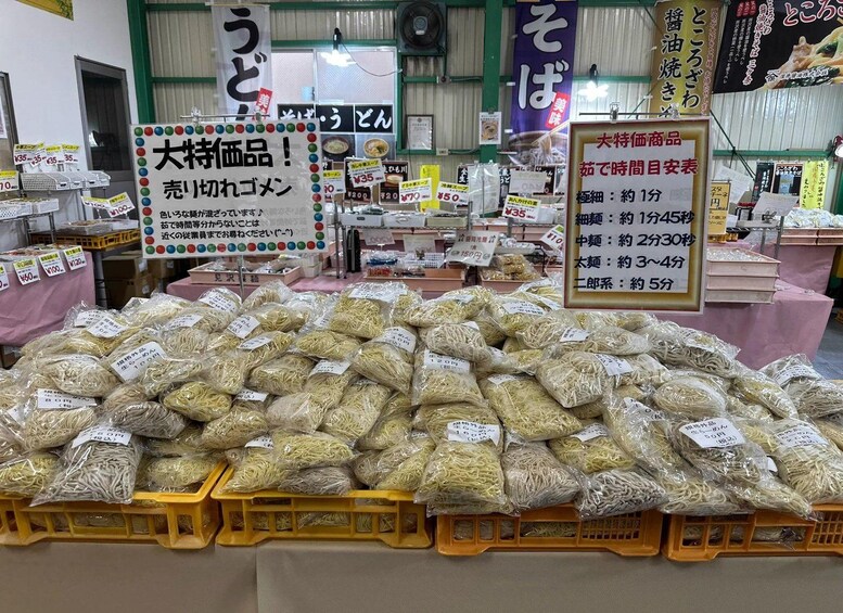 Un puesto de mercado con varios productos envasados, incluyendo fideos, y letreros con texto en japonés. 1