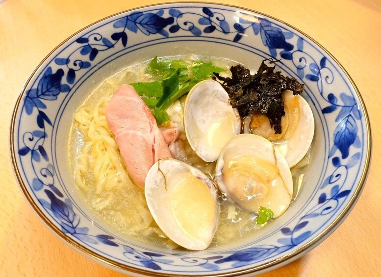 Un tazón de ramen con fideos, almejas, una porción de carne y algas. 3