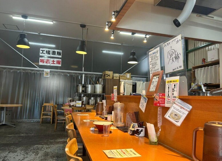 Interior de restaurante con mesas y sillas de madera, luces colgantes y varios carteles y menús. 2