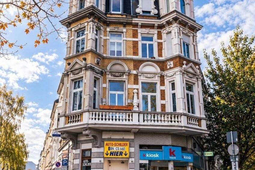 A multi-story building with a balcony, storefronts including a kiosk and a store named 'kiosk,' and a sign for 'AUTO-SCHLUDER.' 2