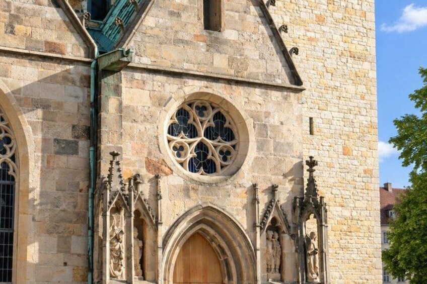 A historic stone building with a large wooden door, arched windows, and intricate stone carvings. 3