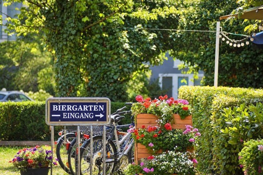 A sign for Biergarten Eingang, a bicycle, and a planter with flowers. 5