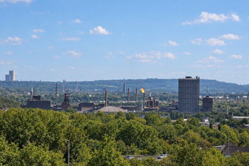 A cityscape with industrial buildings, a large dome structure, and a clear blue sky. 3