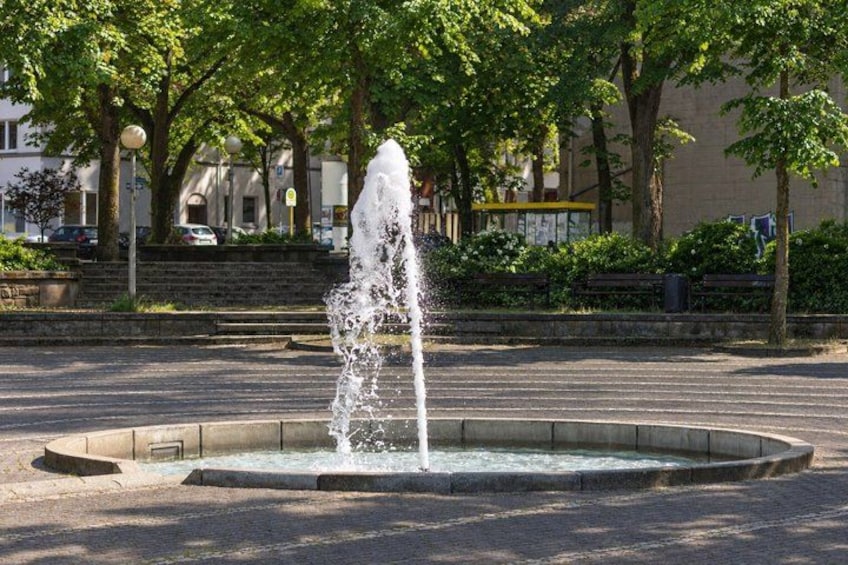 A fountain in a circular basin with water jets, surrounded by trees and a paved area. 2