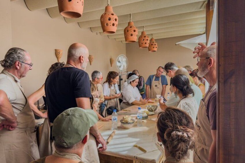 A group of people engaged in a cooking activity around a table with cooking utensils and ingredients. 1