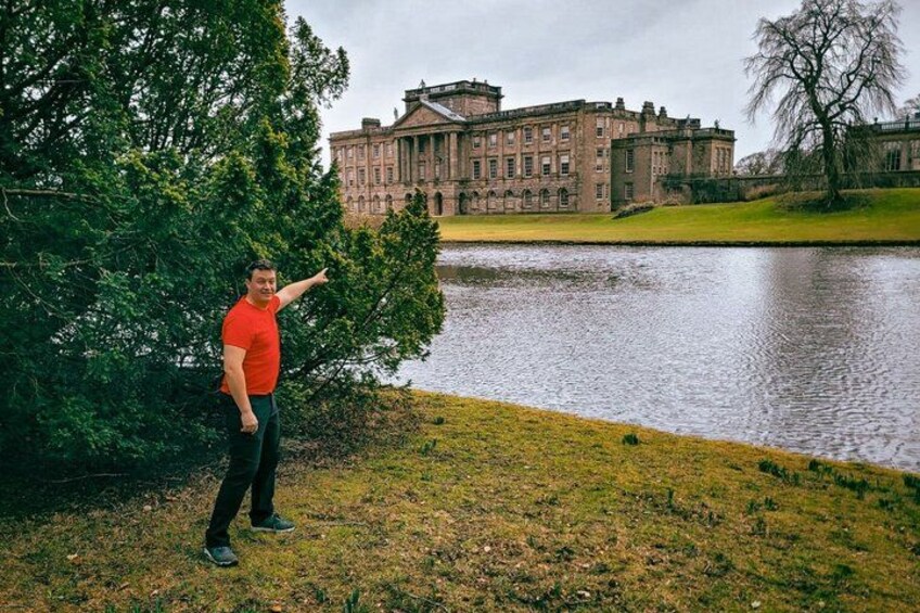 A man in a red shirt pointing towards a large building by a lake. 1