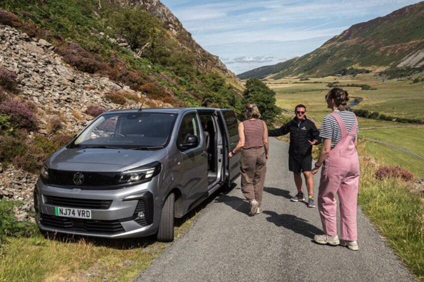 A silver van parked on a rural road with a hilly landscape in the background. 5