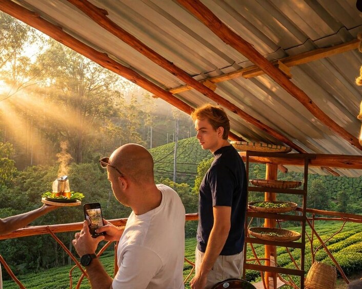 A person holding a tray with a cup and a teapot, another person taking a photo, and a wooden rack with baskets. 5