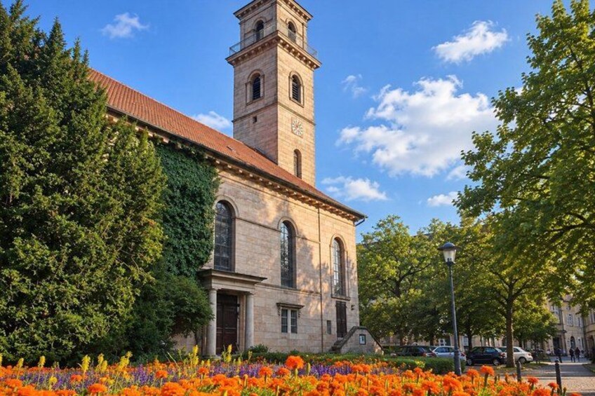 A historic building with a clock tower, surrounded by trees and a flower bed. 5