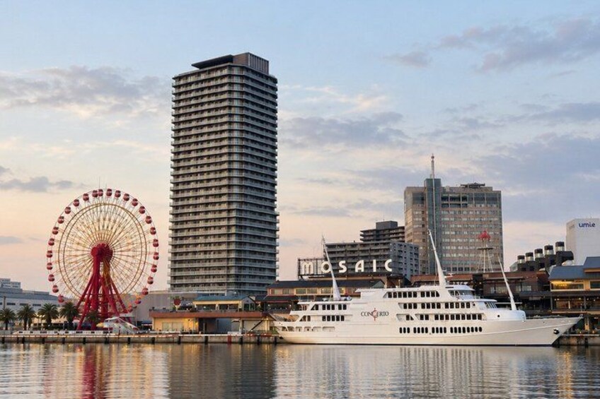 A waterfront cityscape with a Ferris wheel, a tall building, and a cruise ship docked at a marina. 1