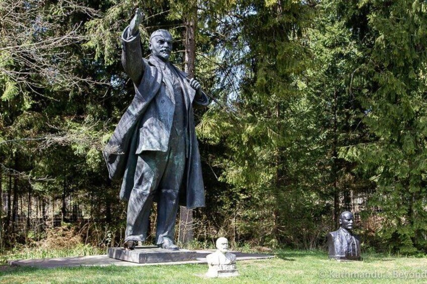 A statue of a man in a suit with his hand raised, surrounded by trees. 3