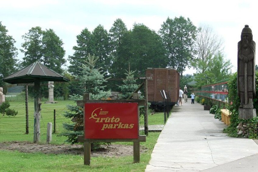 A park entrance with a red sign, a pathway, a gazebo, and a statue. 4