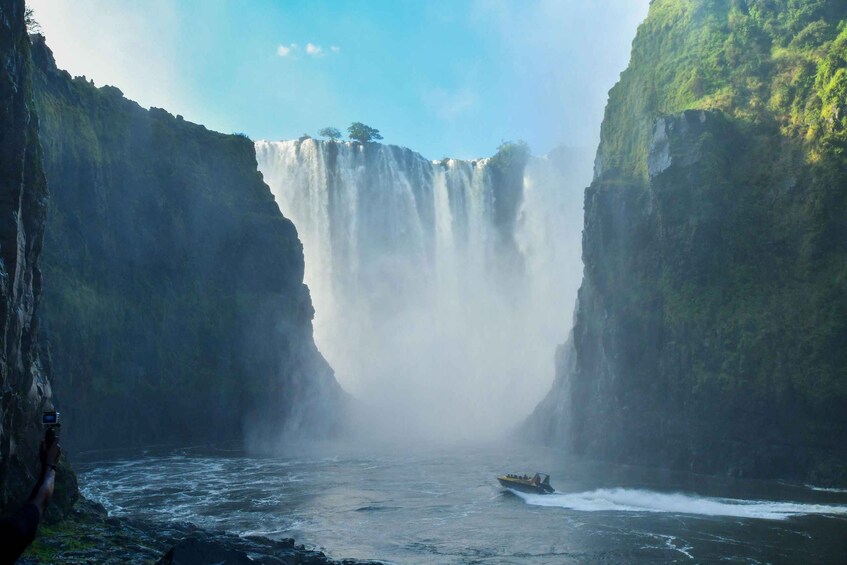A waterfall cascading down a steep cliff into a river, with a boat navigating the water below. 1