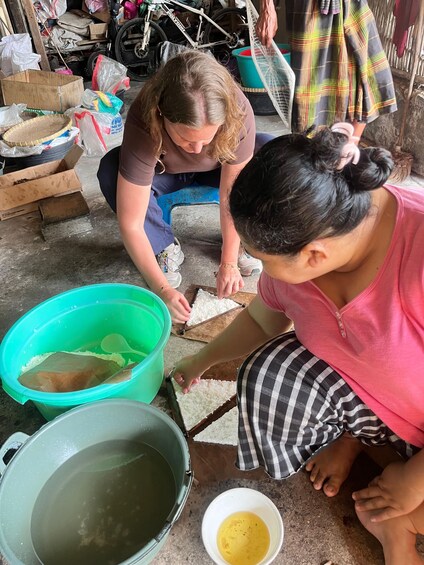 Dos personas arrodilladas sobre un piso de concreto, manipulando arroz y un recipiente de plástico verde. 3