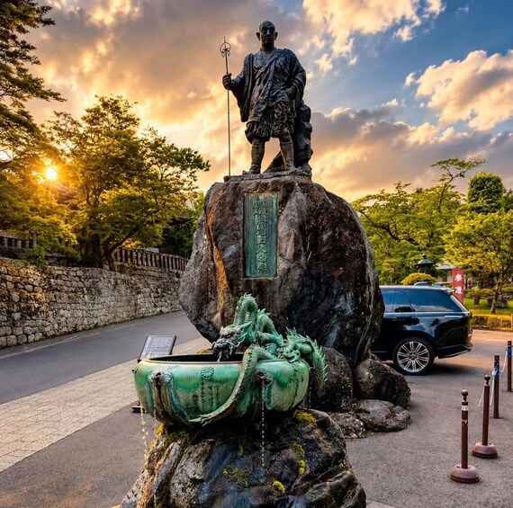 Una estatua sobre una roca con una placa, una escultura de dragón y un coche al fondo. 5