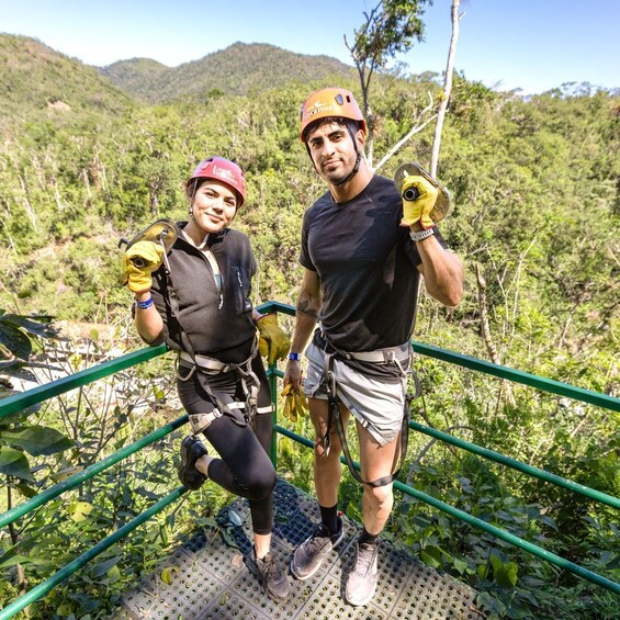 Dos personas con equipo de seguridad sobre un puente colgante, con un paisaje montañoso al fondo. 3
