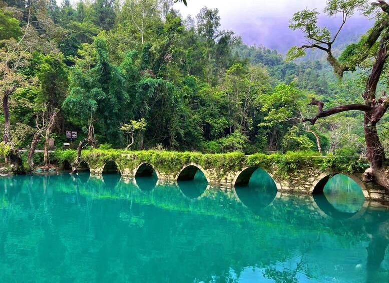 Un río turquesa con un puente de piedra, rodeado de vegetación exuberante y árboles. 4