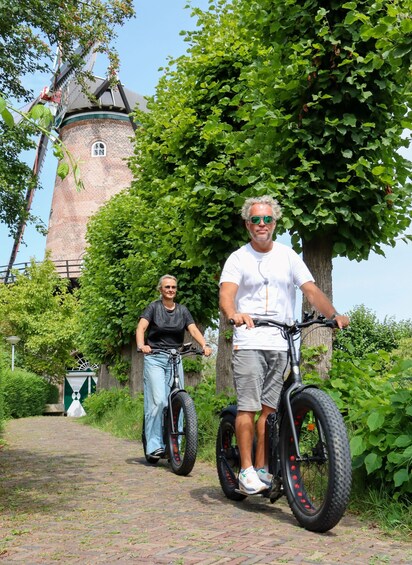 Zwei Personen fahren auf E-Einrädern einen Pflasterweg entlang, im Hintergrund eine Backsteintur und grüne Vegetation. 1