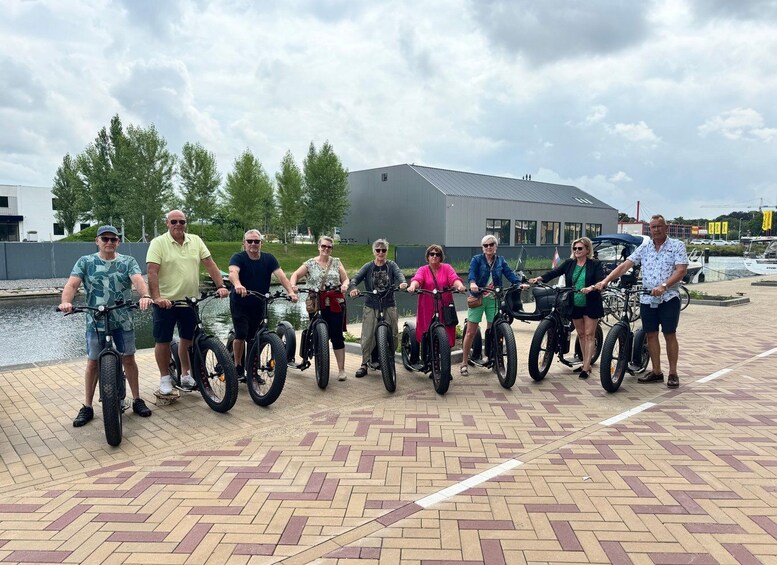 Eine Gruppe von Menschen fährt mit E-Bikes in einer offenen Landschaft, im Hintergrund sind ein Gewässer und Gebäude zu sehen. 4