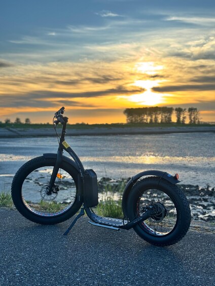 Ein stehender Elektroscooter auf einer Straße, im Hintergrund ein Sonnenuntergang. 2