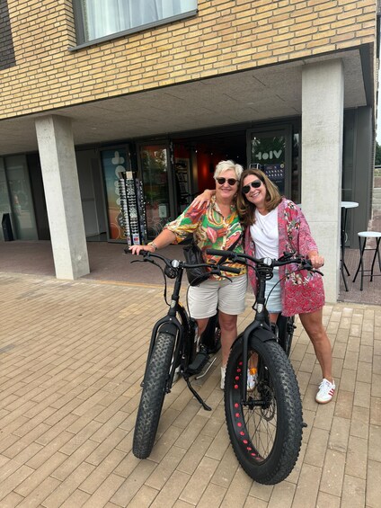 Zwei Personen fahren mit E-Bikes vor einem Gebäude mit Backsteinfassade und Glastür. 5