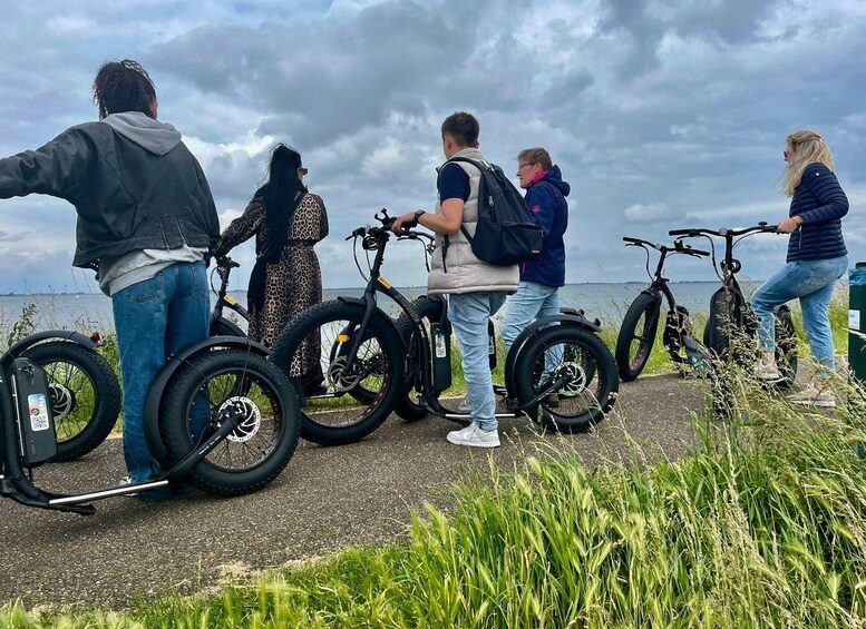 Eine Gruppe von Menschen steht in der Nähe von Fahrrädern an einem Gewässer, der Himmel ist bewölkt. 3