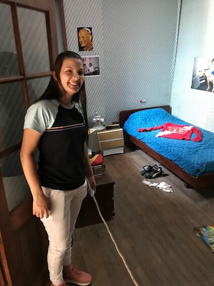 Une personne se tient dans une pièce où se trouve un lit, une couverture bleue et une chemise rouge posée sur le lit. 2