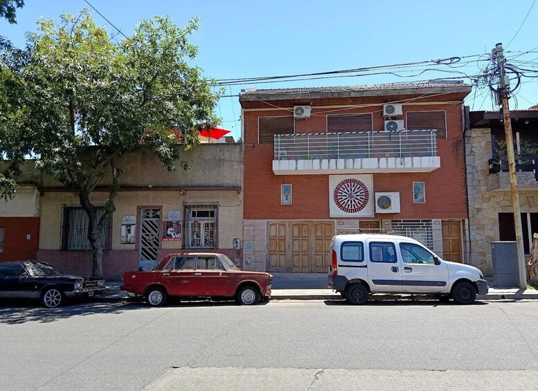 Une scène de rue avec une voiture rouge garée sur le bord, un fourgon blanc devant, et un immeuble à la façade rouge et blanche. 4